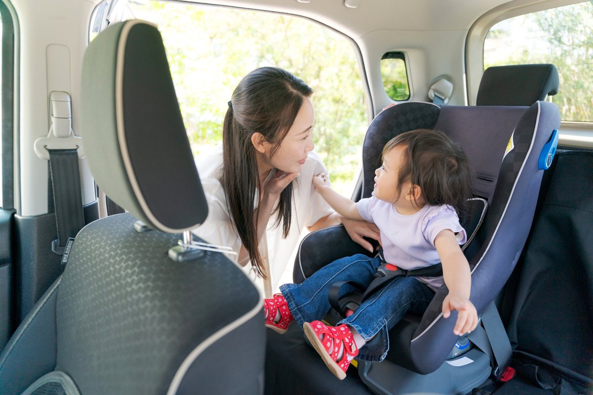 車内で、チャイルドシートに座る子どもと向き合う母親
