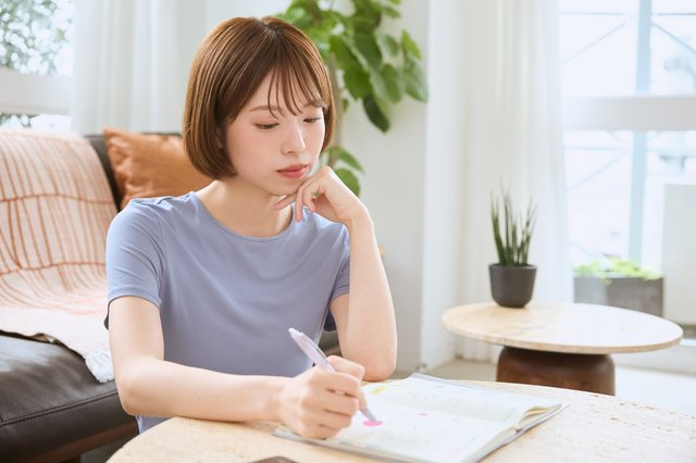 リビングでノートに書き込みながら考え込む女性